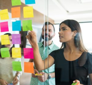 Female young manager discussing over adhesive note with coworkers in office meeting